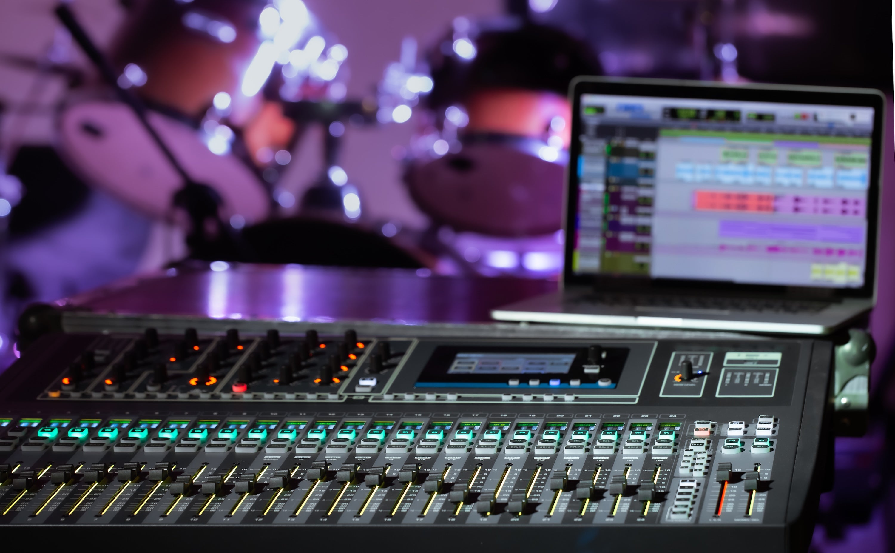 Mixing board with laptop and drums in the back